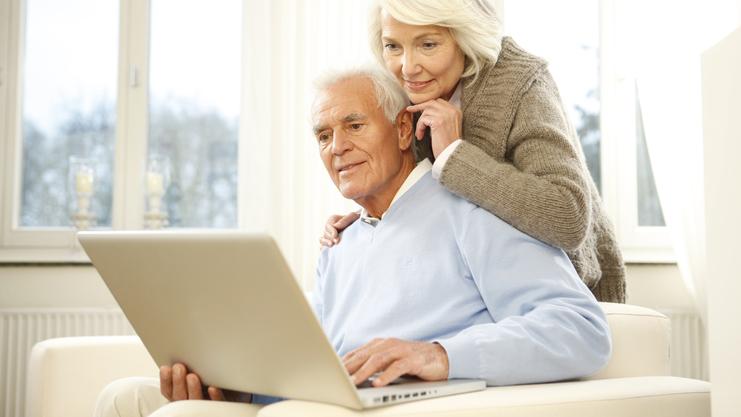 Paar sitzt auf einer Couch und schaut gemeinsam auf einen Laptop in einem hellen Raum.